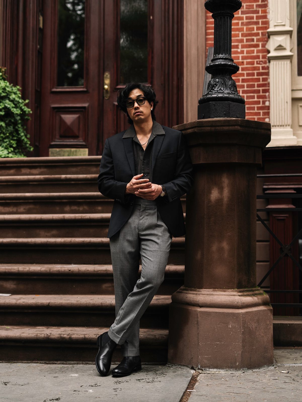 Man in a black blazer, grey trousers, and black Chelsea boots posing on stone steps.