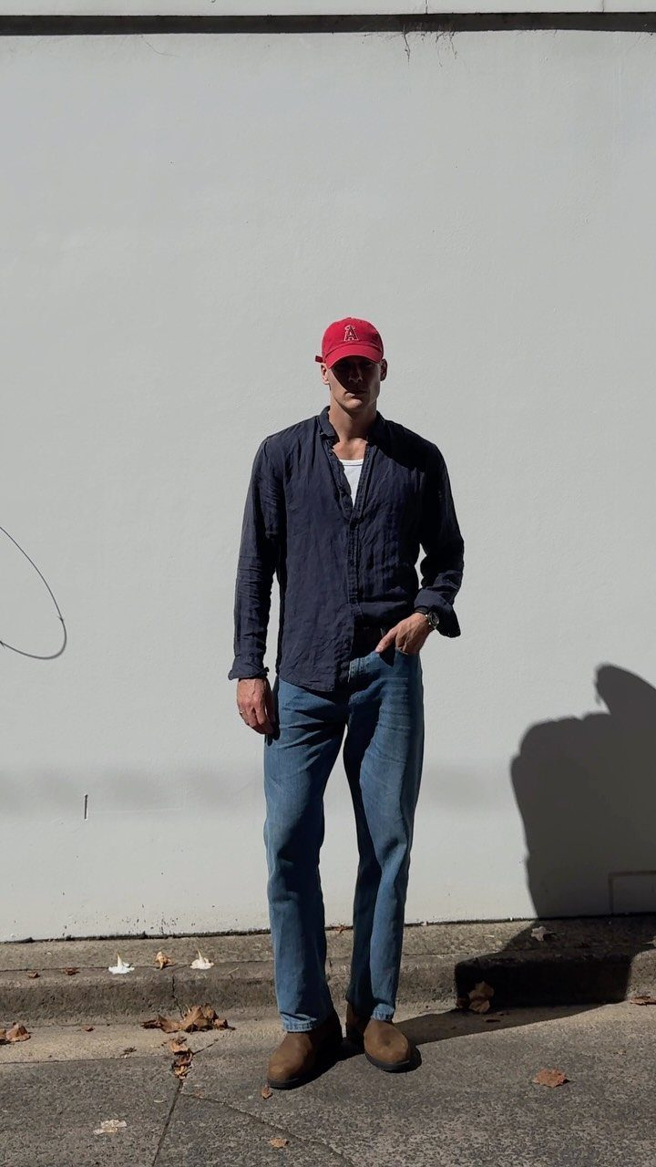 Man wearing a navy button-down shirt, blue jeans, and brown suede Chelsea boots.