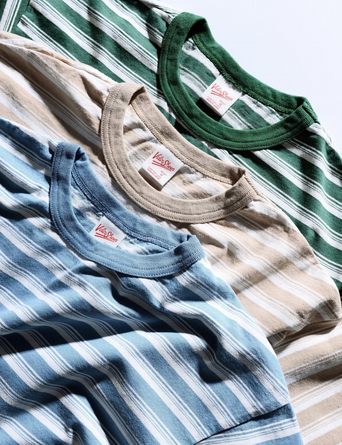 Three striped crewneck t-shirts in blue, beige, and green layered on a white background.