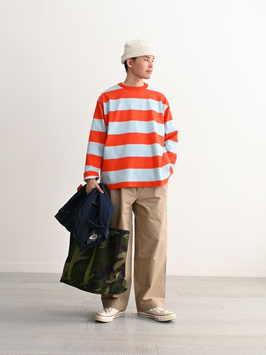 A person in a striped orange and blue shirt and tan pants holding bags.
