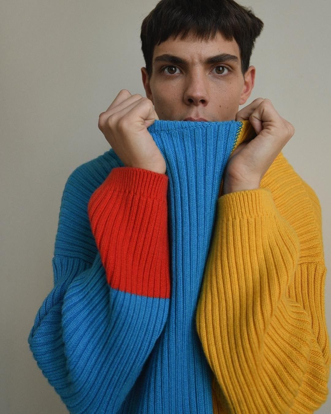 A person wearing a bright, color-blocked blue, red, and yellow ribbed knit sweater.