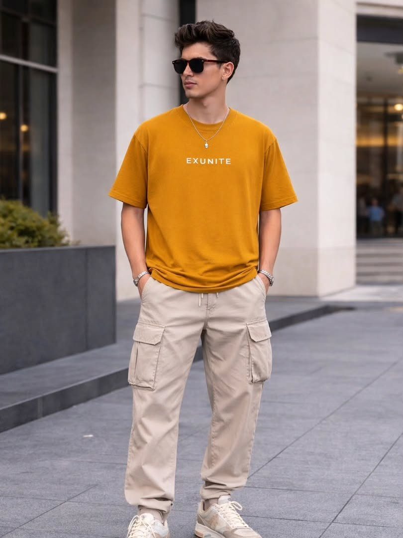 A man wearing a mustard yellow t-shirt and beige cargo pants standing outdoors.