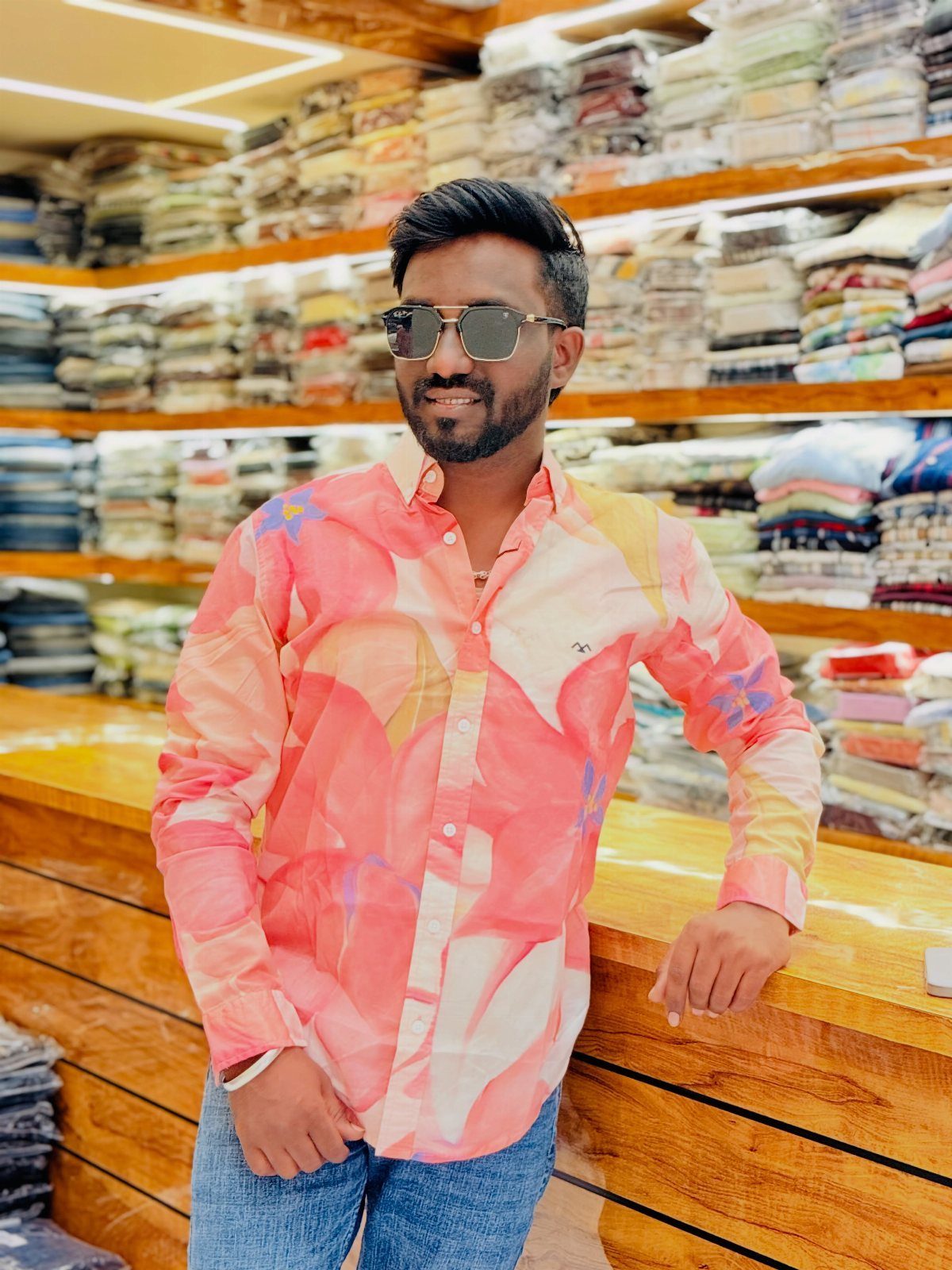 Man in a pink floral printed linen shirt and blue jeans standing in a clothing store.