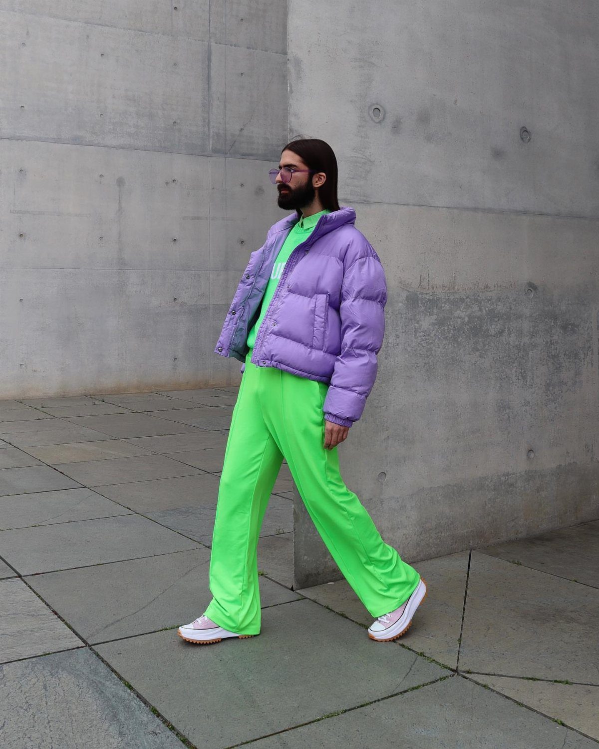 Man walking in a bright lime green outfit paired with a lavender puffer jacket and white sneakers.