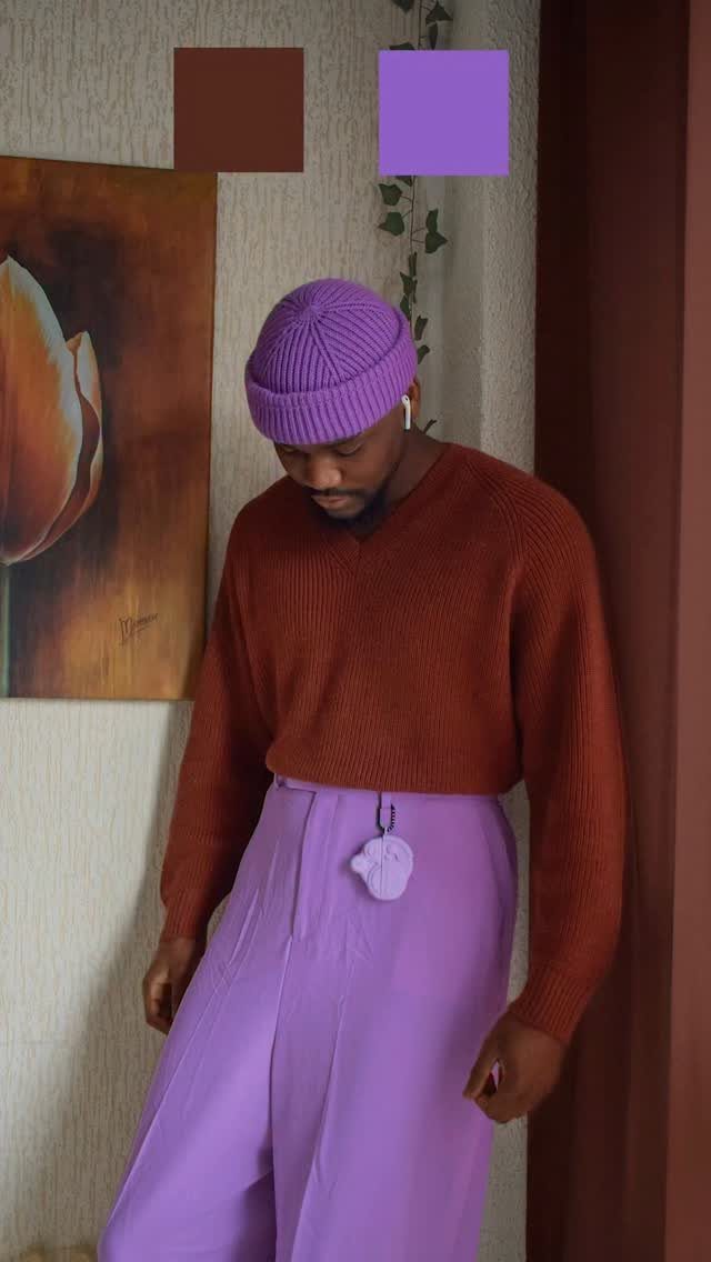 Man wearing a burnt orange sweater with bright purple trousers and a purple beanie.