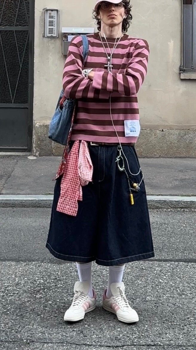 Man wearing a pink and brown striped shirt with dark denim shorts and pink sneakers.