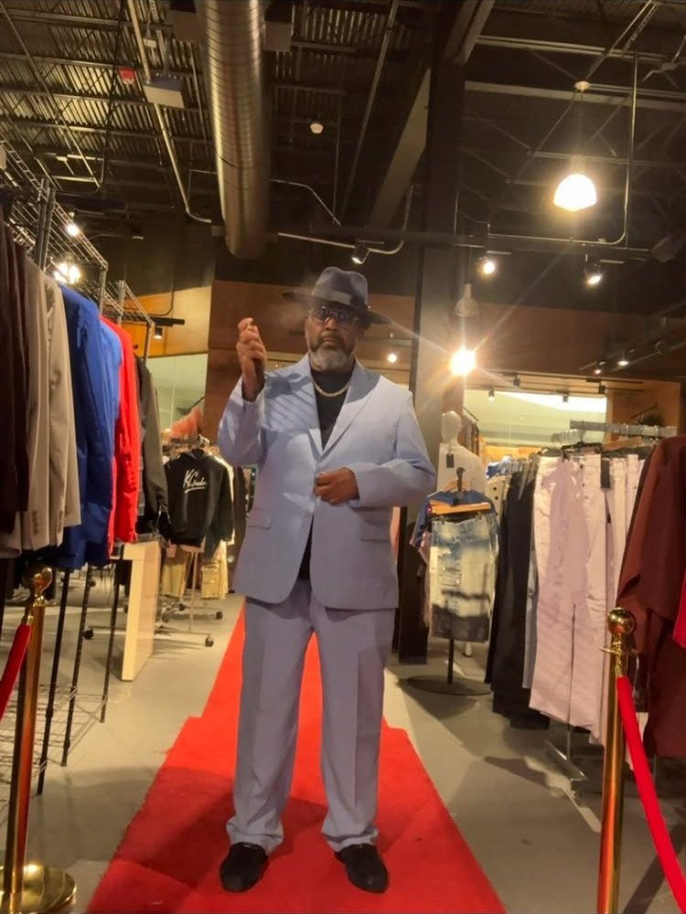 Man in a light blue suit and hat posing on a red carpet in a store.