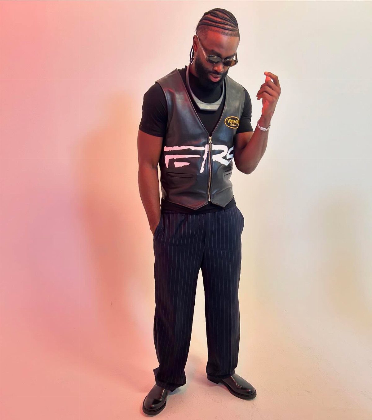 Man posing in a black leather vest, black t-shirt, and pinstriped trousers.