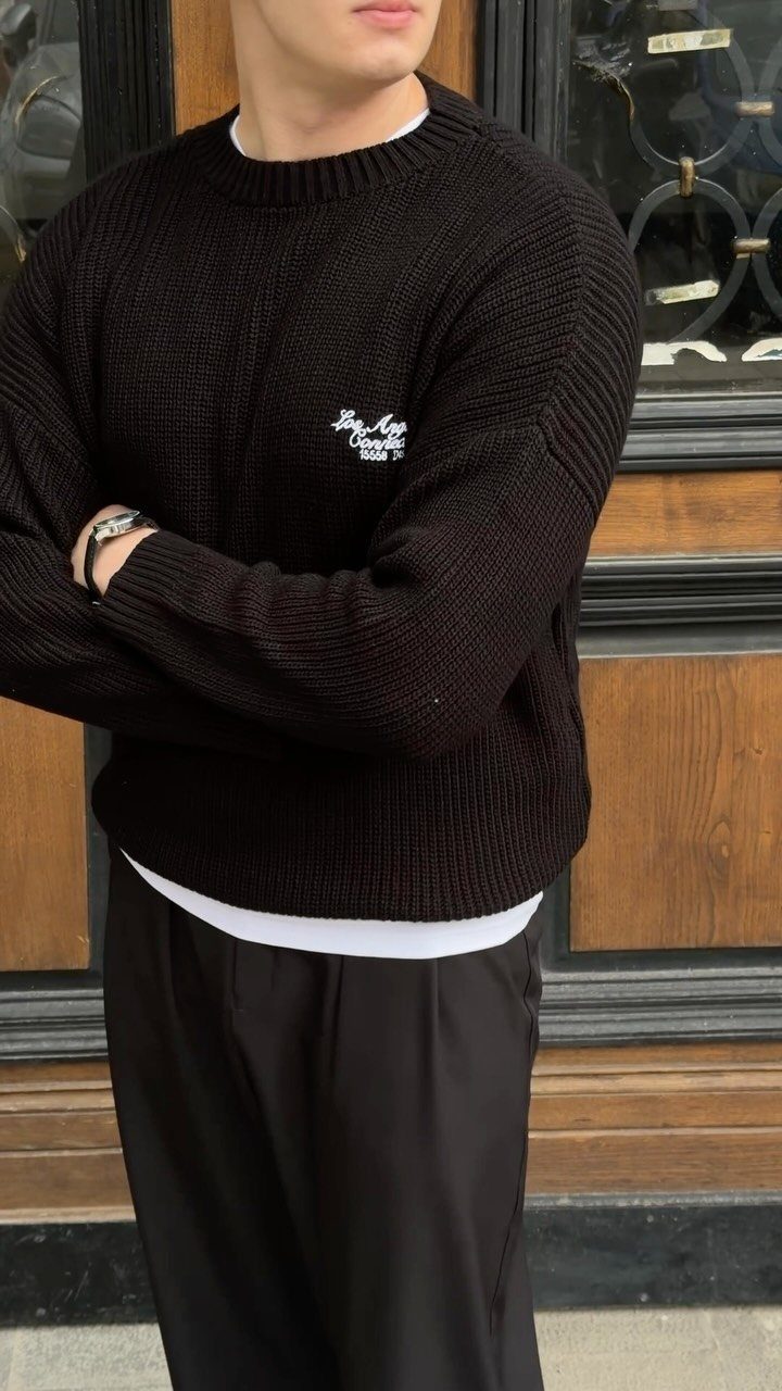 Man wearing a textured black long-sleeve crewneck sweater with white text on the chest.