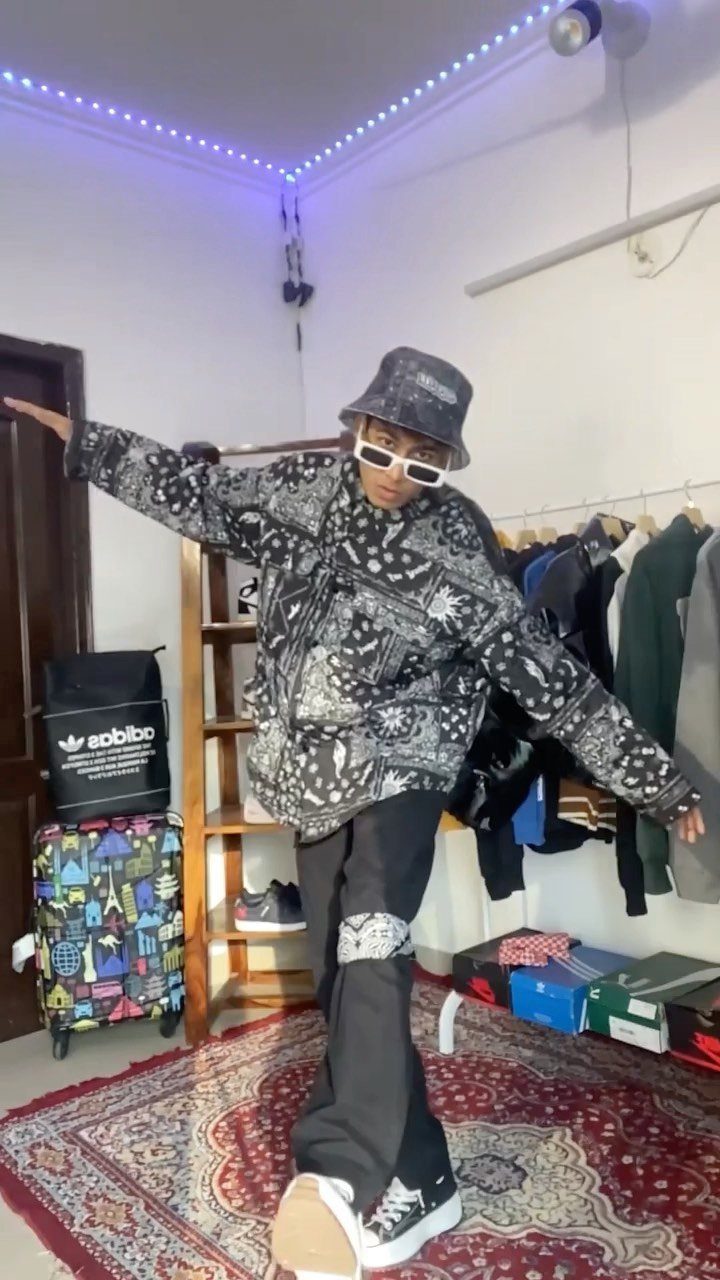 Man posing in a black and white patterned hoodie, black pants, and a patterned bucket hat.