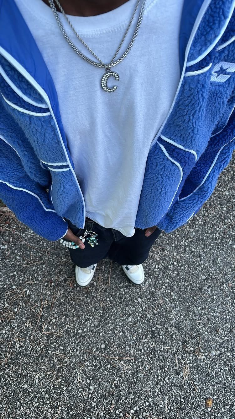 A person wearing a blue fleece jacket, silver chains, white t-shirt, and white sneakers.