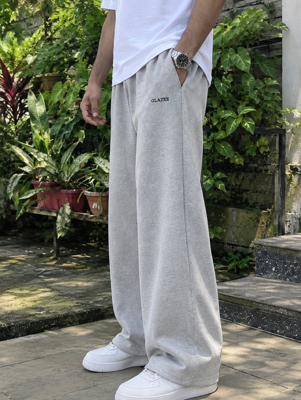 A person wearing light grey wide-leg sweatpants and white sneakers in a garden.