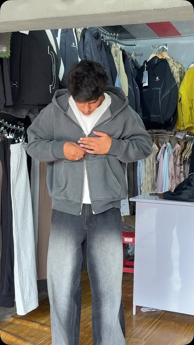 A man wearing a grey oversized zip-up hoodie and faded grey jeans.