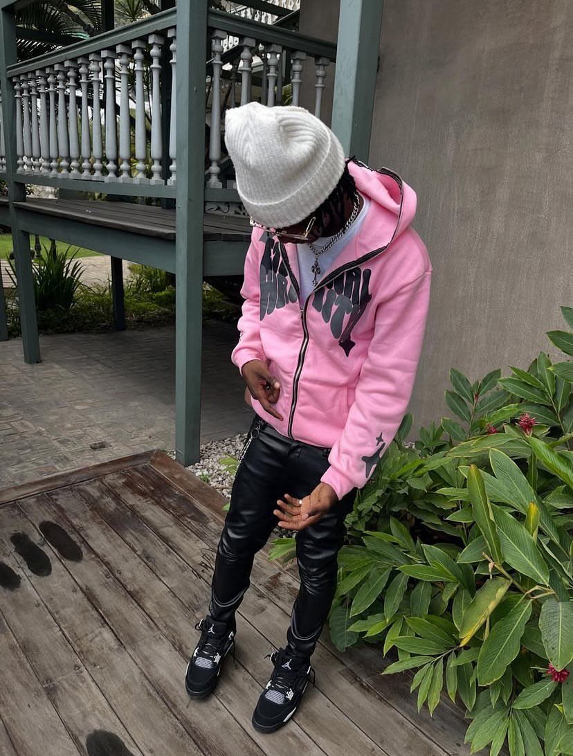 A person in a pink hoodie and black leather-look pants standing on a wooden deck.