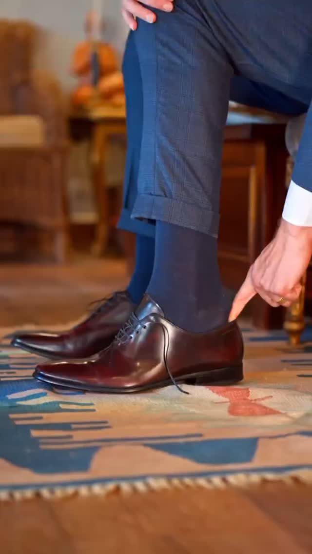 A person pointing to polished dark burgundy leather derby shoes worn with blue trousers.