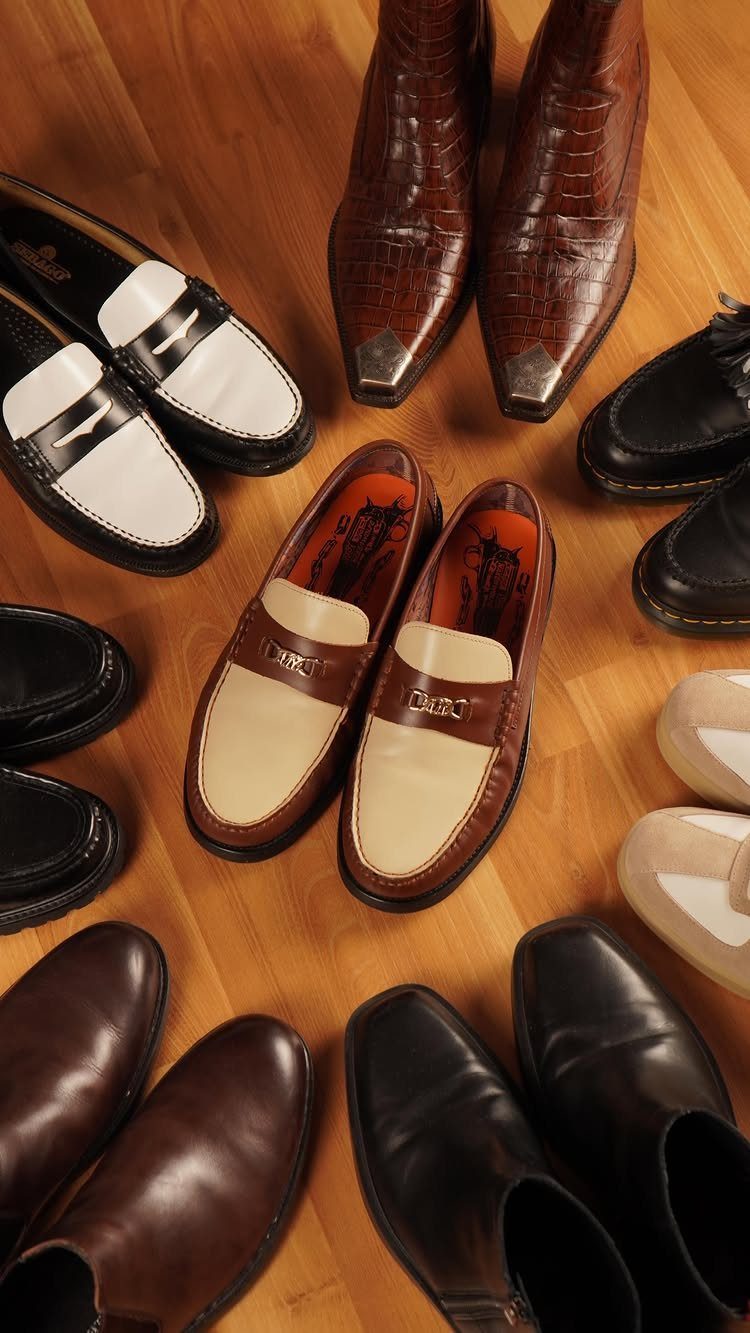 Various men's leather shoes including loafers and boots arranged in a circle on a wooden floor.