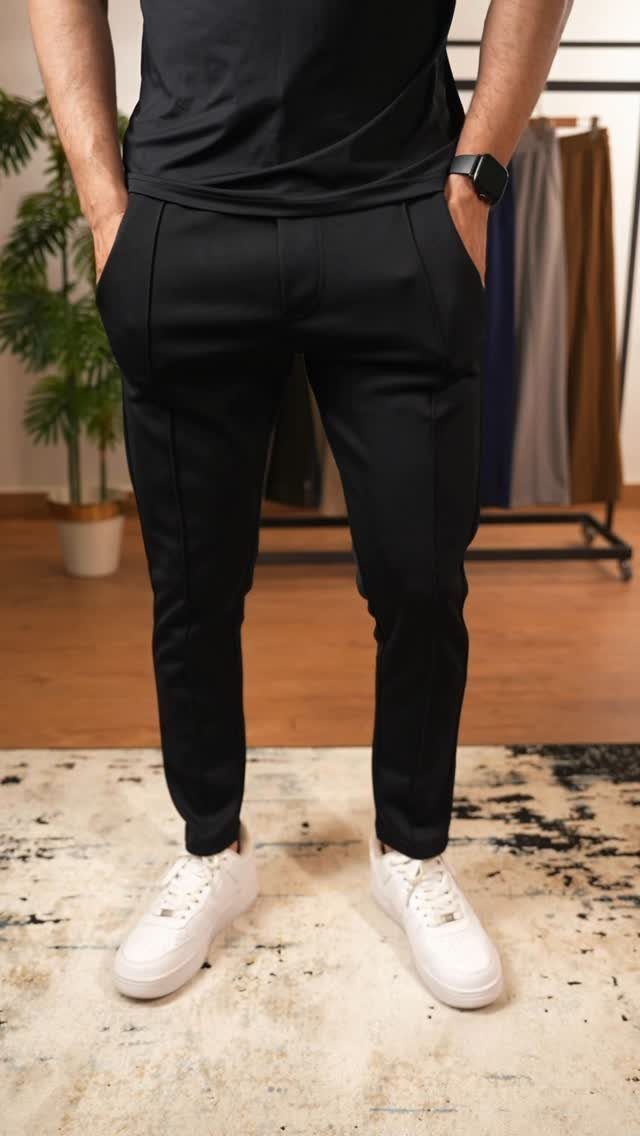 Man wearing a black t-shirt, black trousers, and white sneakers standing on a rug.