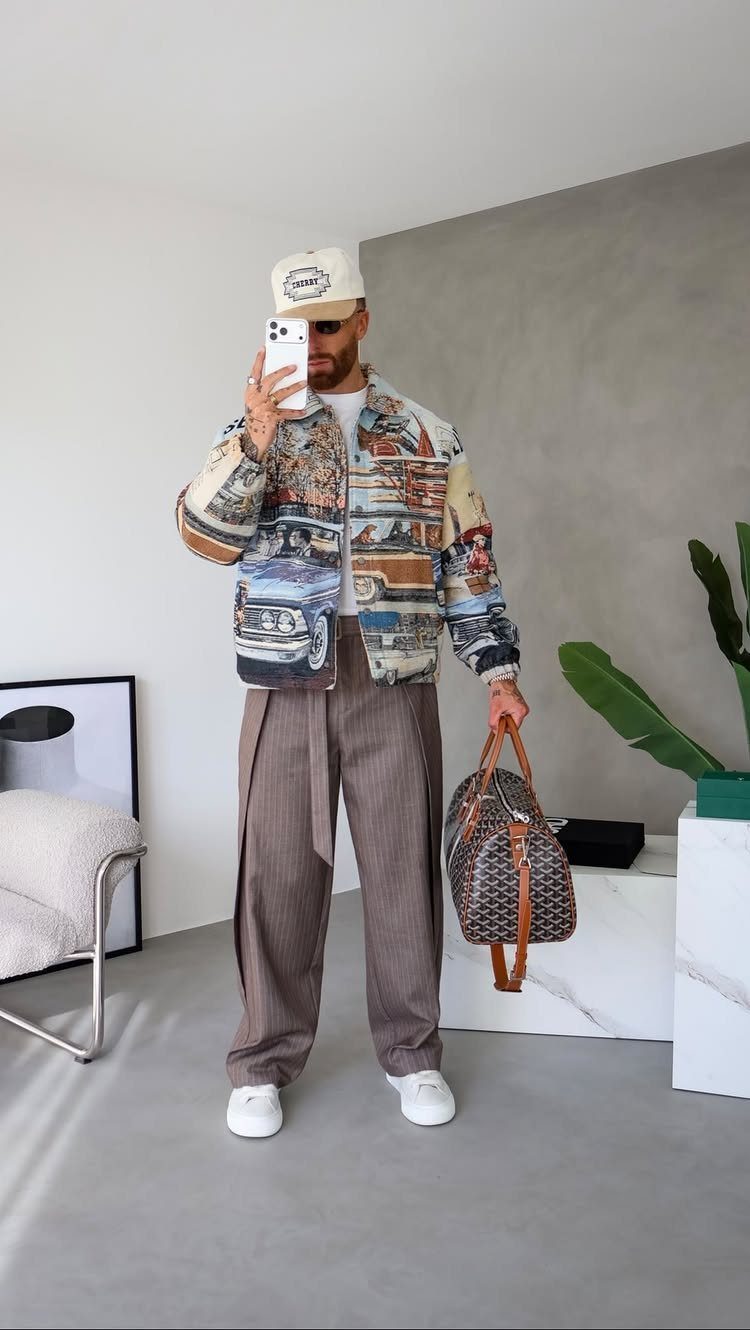 Man in a patterned jacket, brown trousers, and white sneakers posing for a mirror selfie.