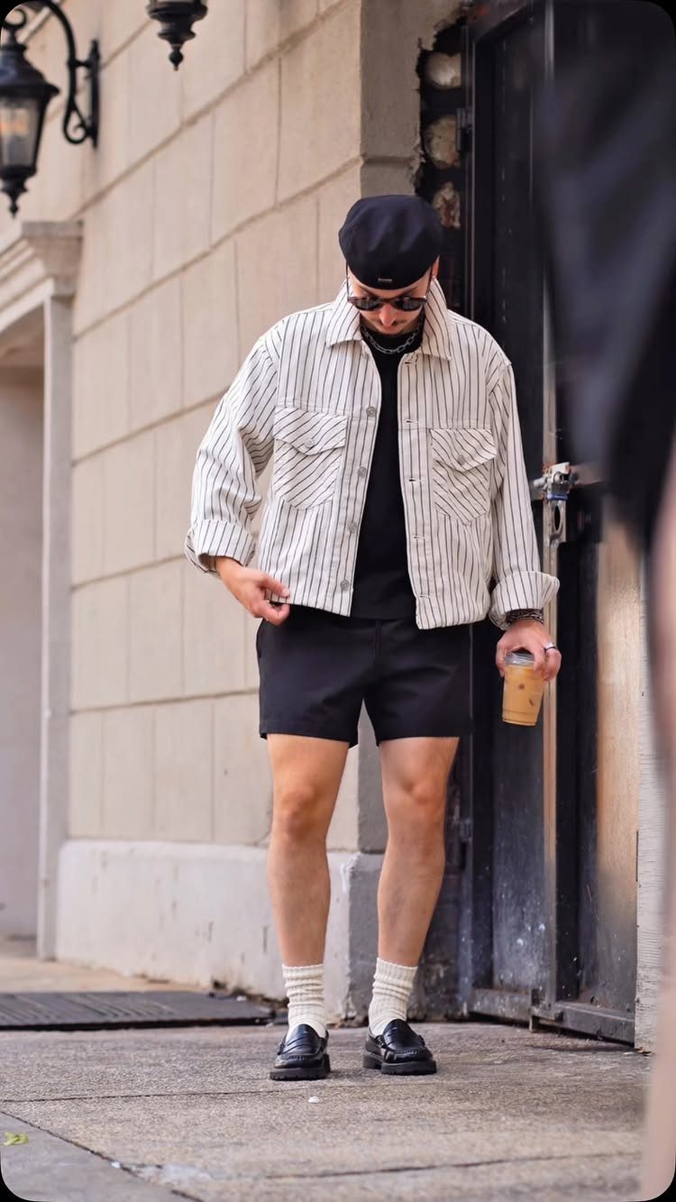 Man in a striped shirt, black shorts, white socks, and black loafers standing outdoors.