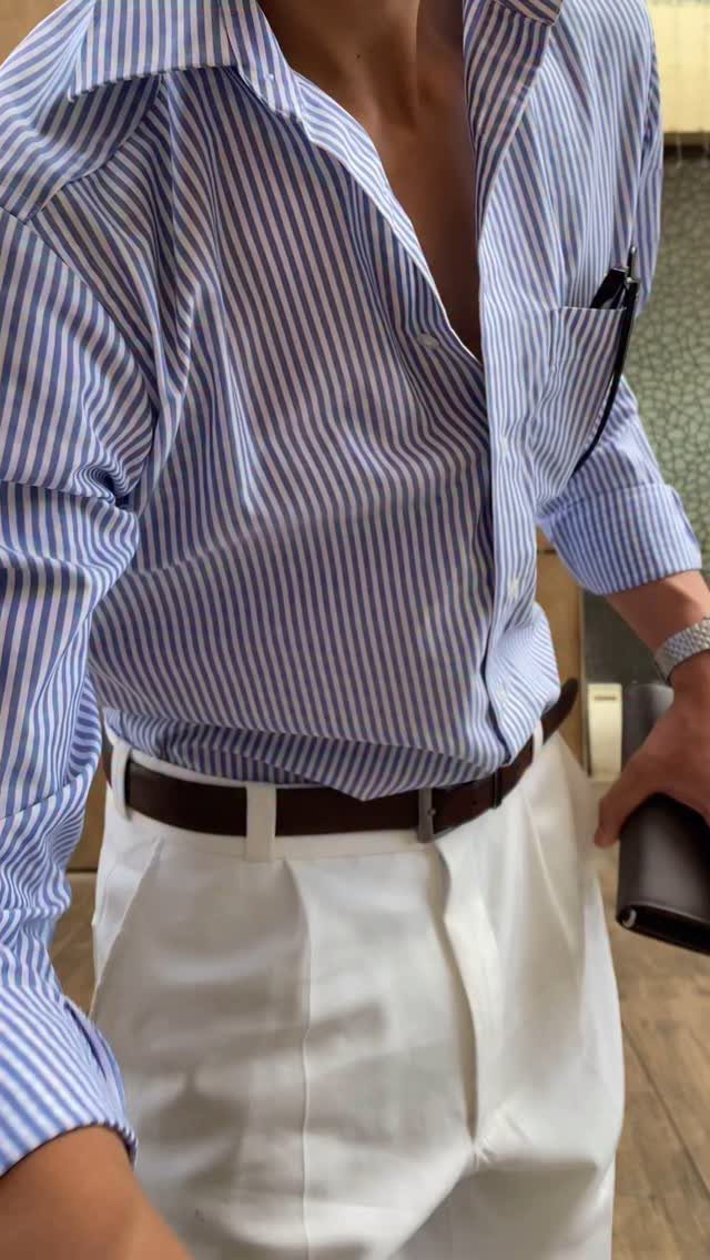 Man wearing a blue and white striped shirt tucked into white trousers with a brown belt.