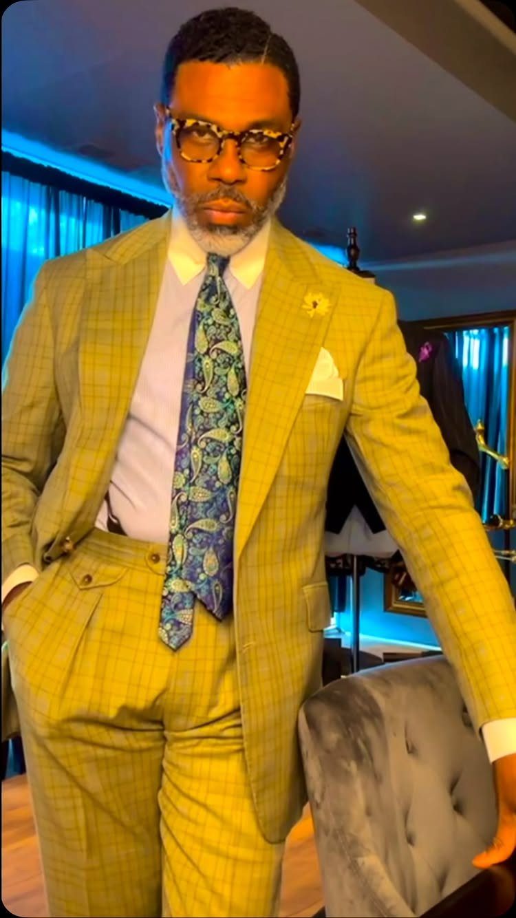A man posing in a yellow plaid blazer and matching trousers with a blue patterned tie.