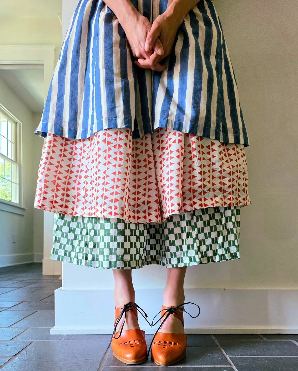 Person wearing a multi-patterned layered skirt with blue stripes, red triangles, and green checkers.