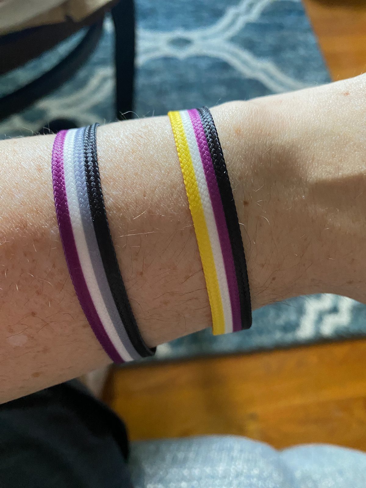 Two striped fabric wristbands in pride colors worn on a person's wrist.