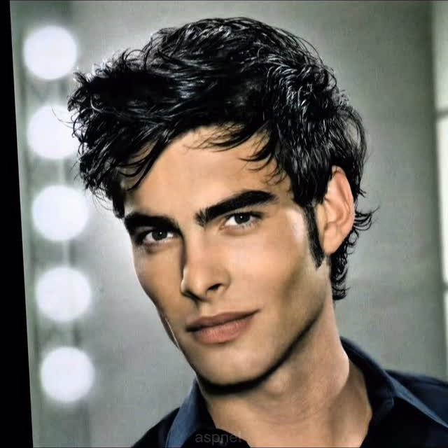 A handsome man with dark wavy hair and thick eyebrows smiling slightly.