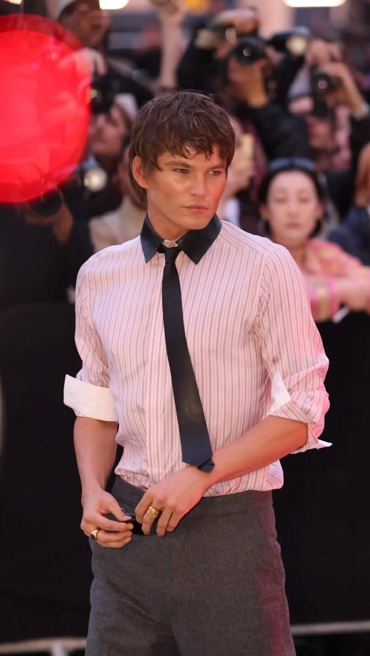 A handsome man in a striped shirt and black tie posing on a red carpet.