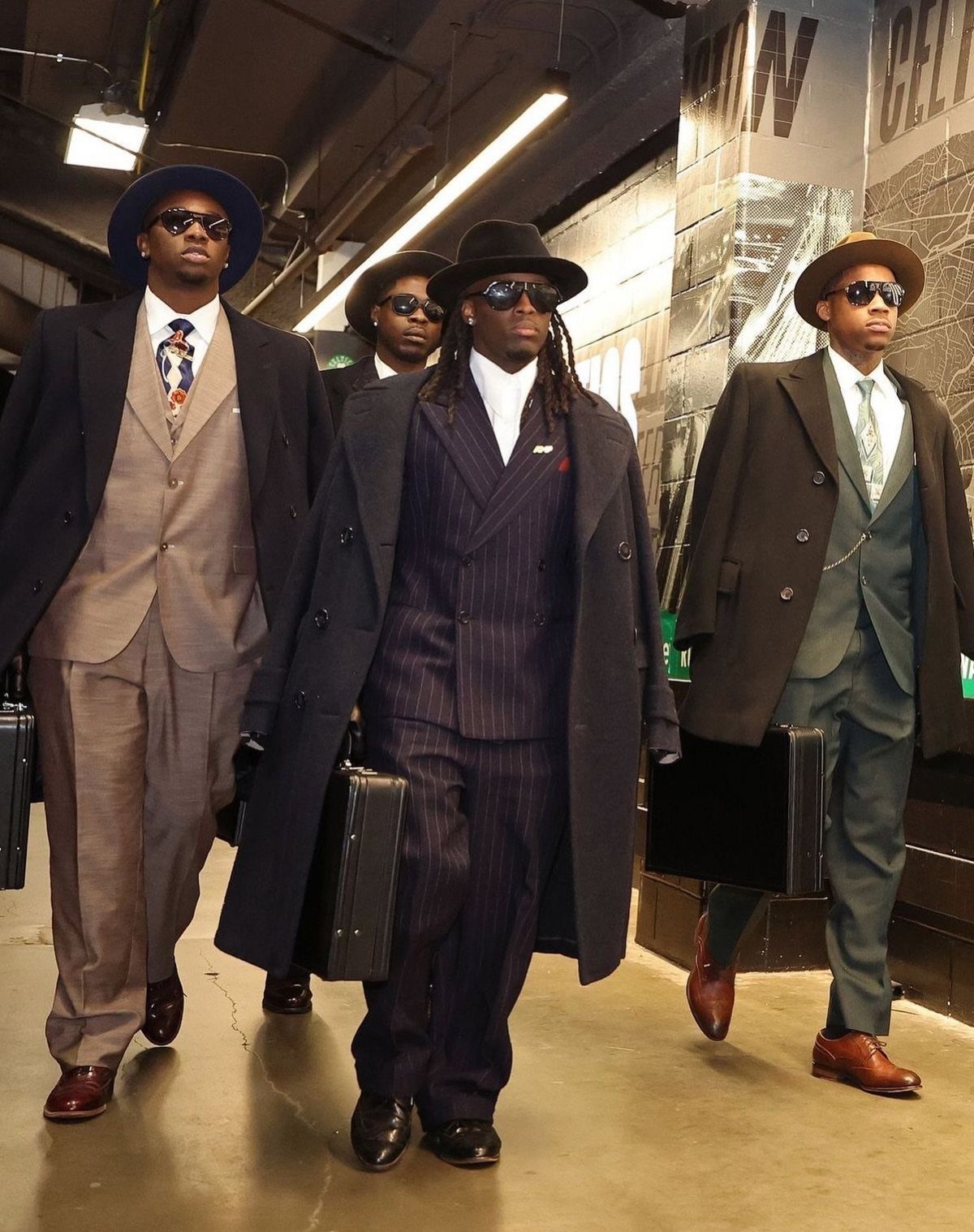 Three men in vintage suits, overcoats, and fedoras walking while carrying black briefcases.