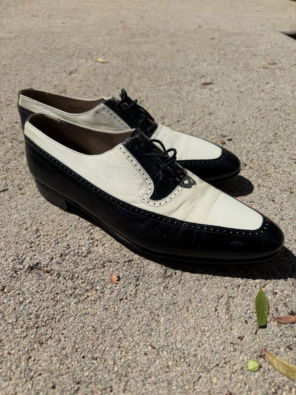 Two-tone black and white spectator shoes resting on a textured concrete ground.