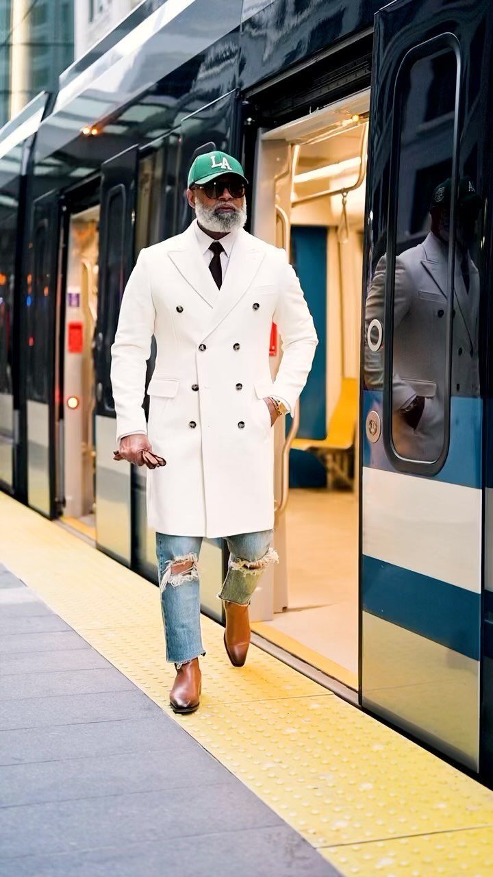 Man in a white double-breasted coat and ripped jeans walking out of a train.