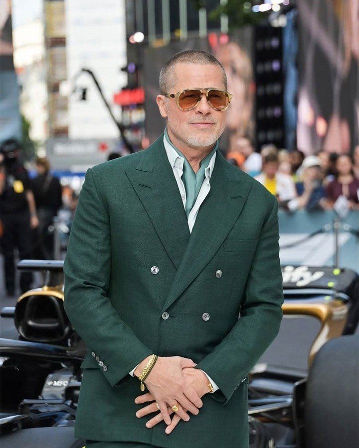 A man in a green double-breasted suit and sunglasses standing in a city setting.
