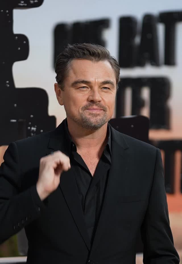 Leonardo DiCaprio wearing a stylish black suit and black shirt while posing for a photo.