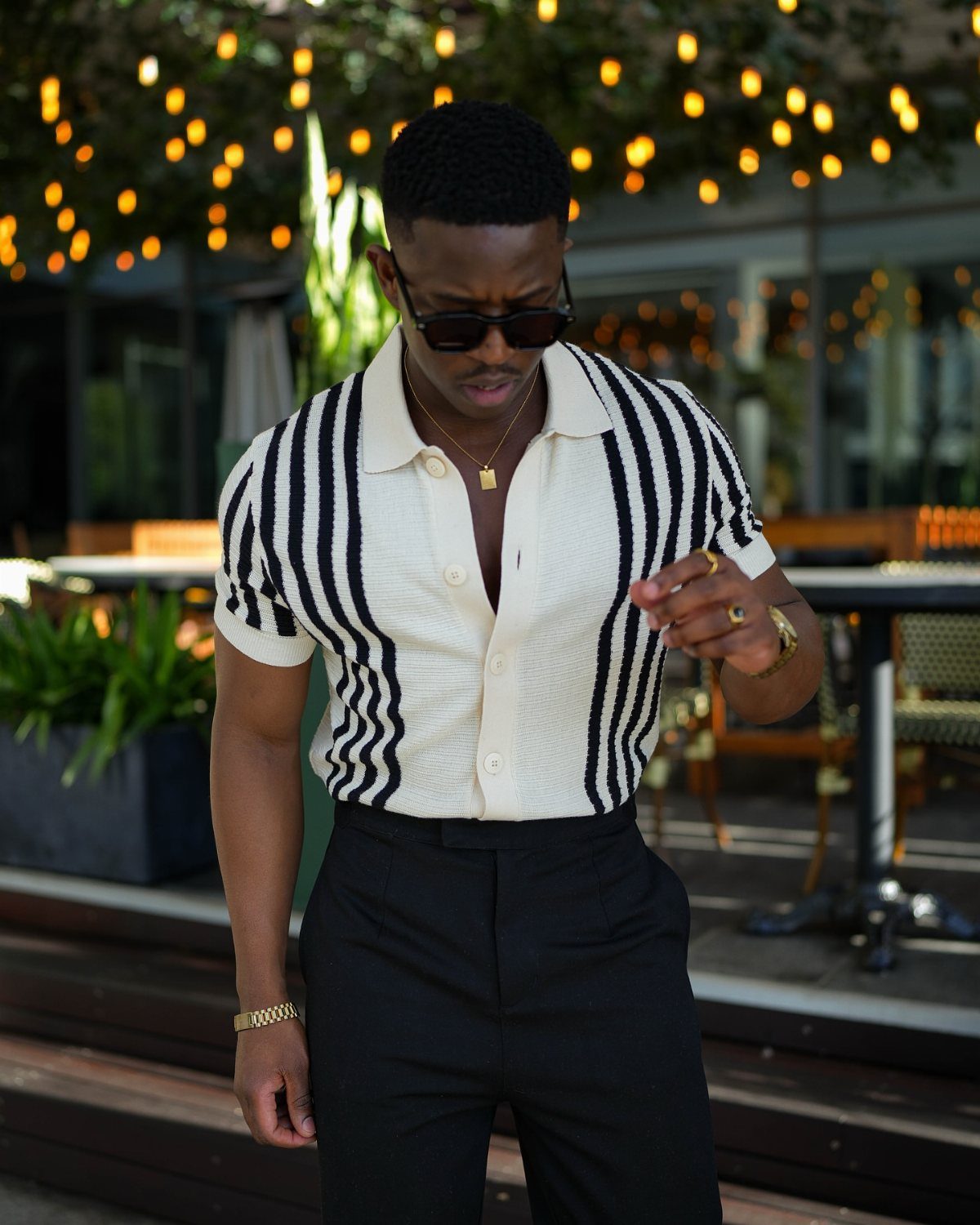 Man wearing a cream and black vertically striped statement polo shirt and black trousers.