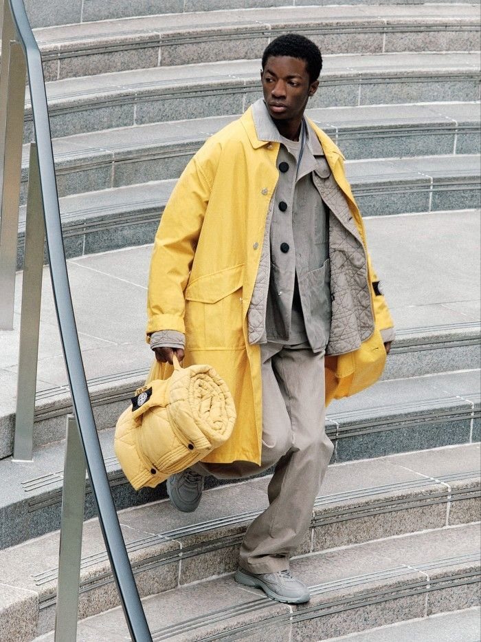 Man in yellow technical raincoat and quilted clothing walking down stone stairs.
