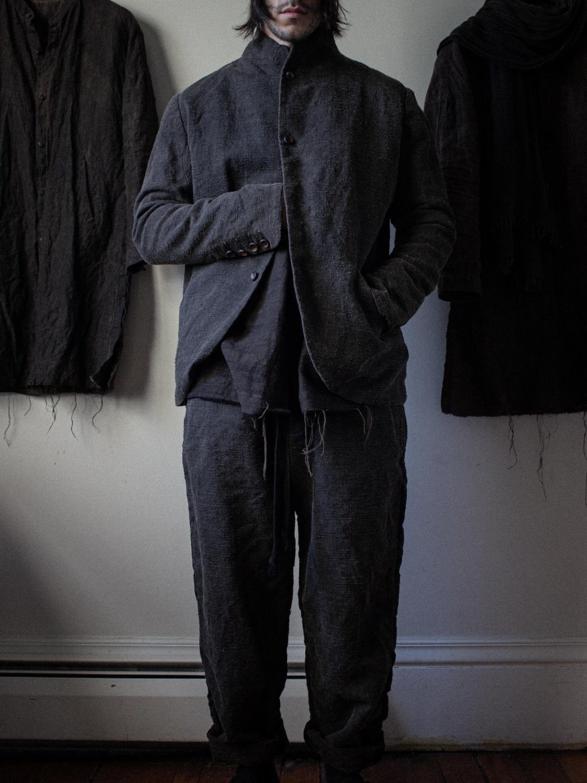 A person wearing a relaxed, dark charcoal grey textured linen suit with wide-leg trousers.