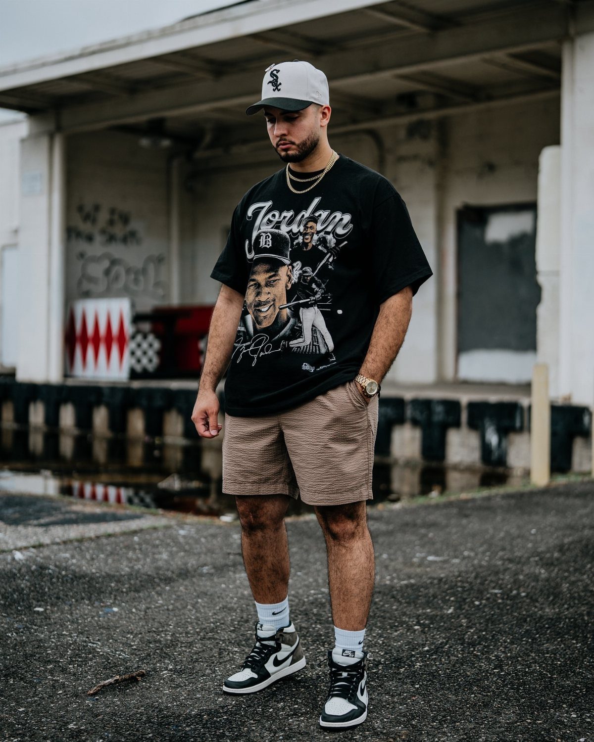 Man wearing a black graphic t-shirt, tan shorts, and black and white high-top sneakers.