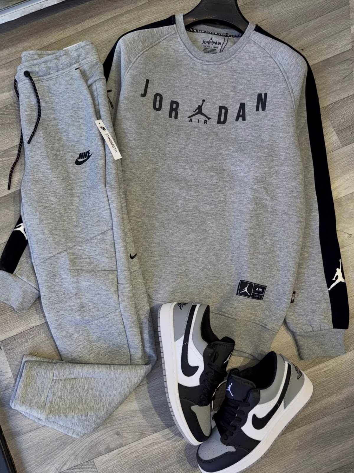 Grey Jordan sweatshirt, matching joggers, and black and white sneakers laid on a wooden floor.