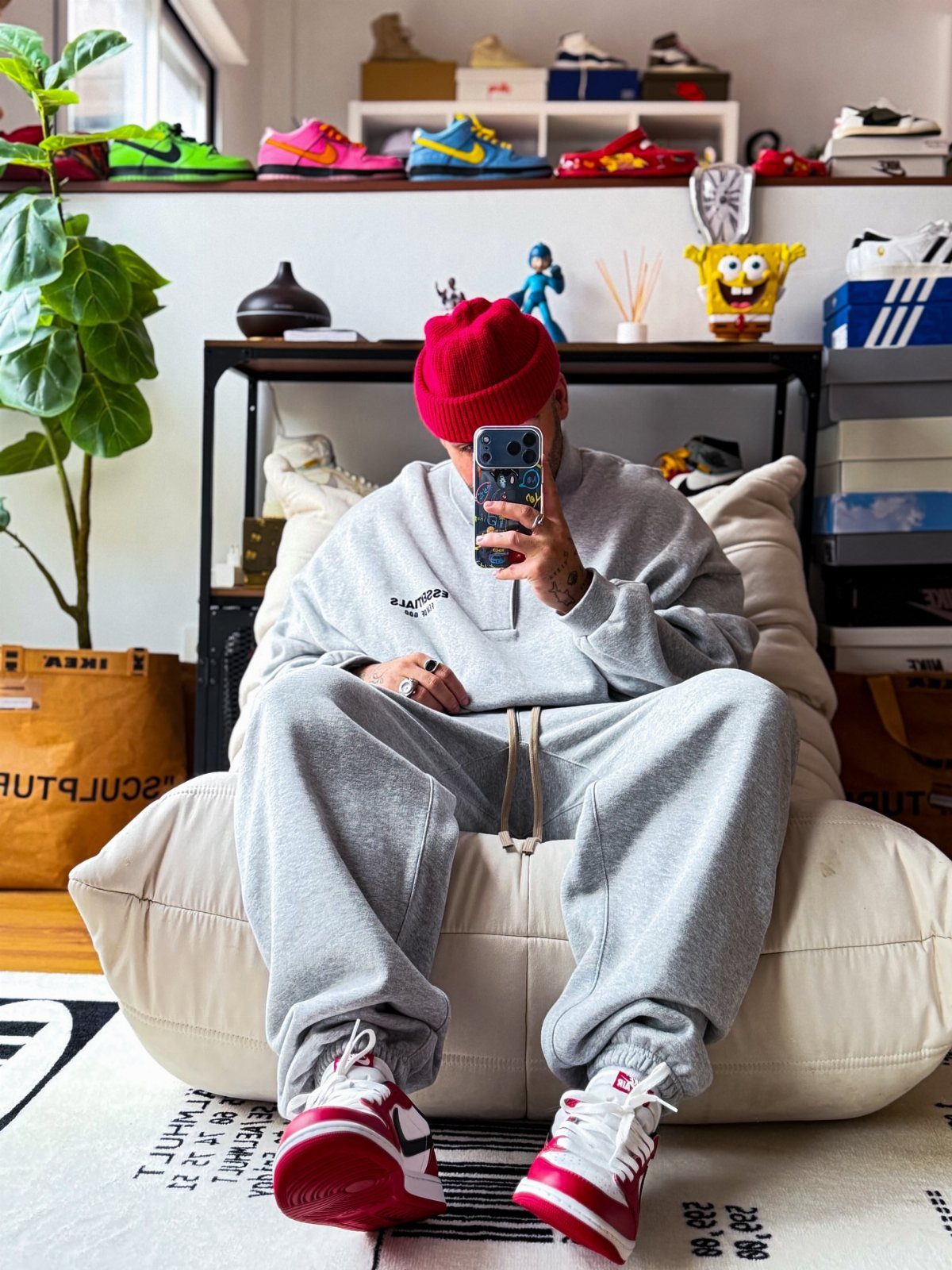 Man in grey sweatshirt and joggers wearing red and white sneakers sitting on a beanbag.