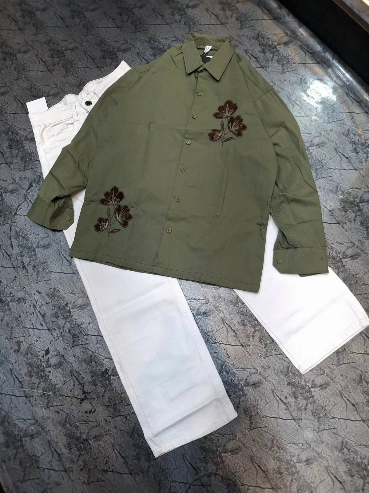 Olive green embroidered shirt and white trousers laid flat on a dark grey surface.