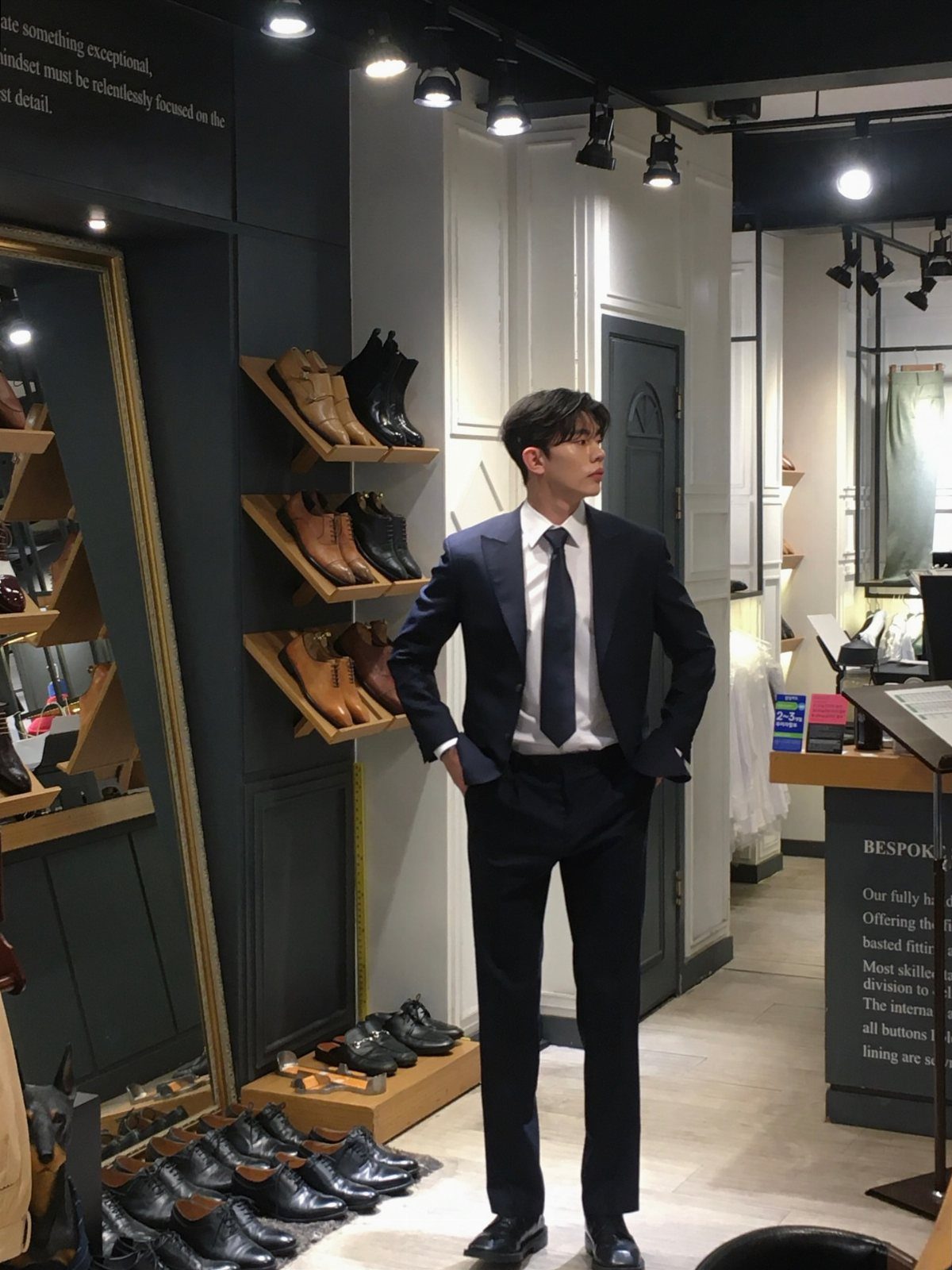 A man posing in a dark navy tailored suit inside a high-end shoe boutique.