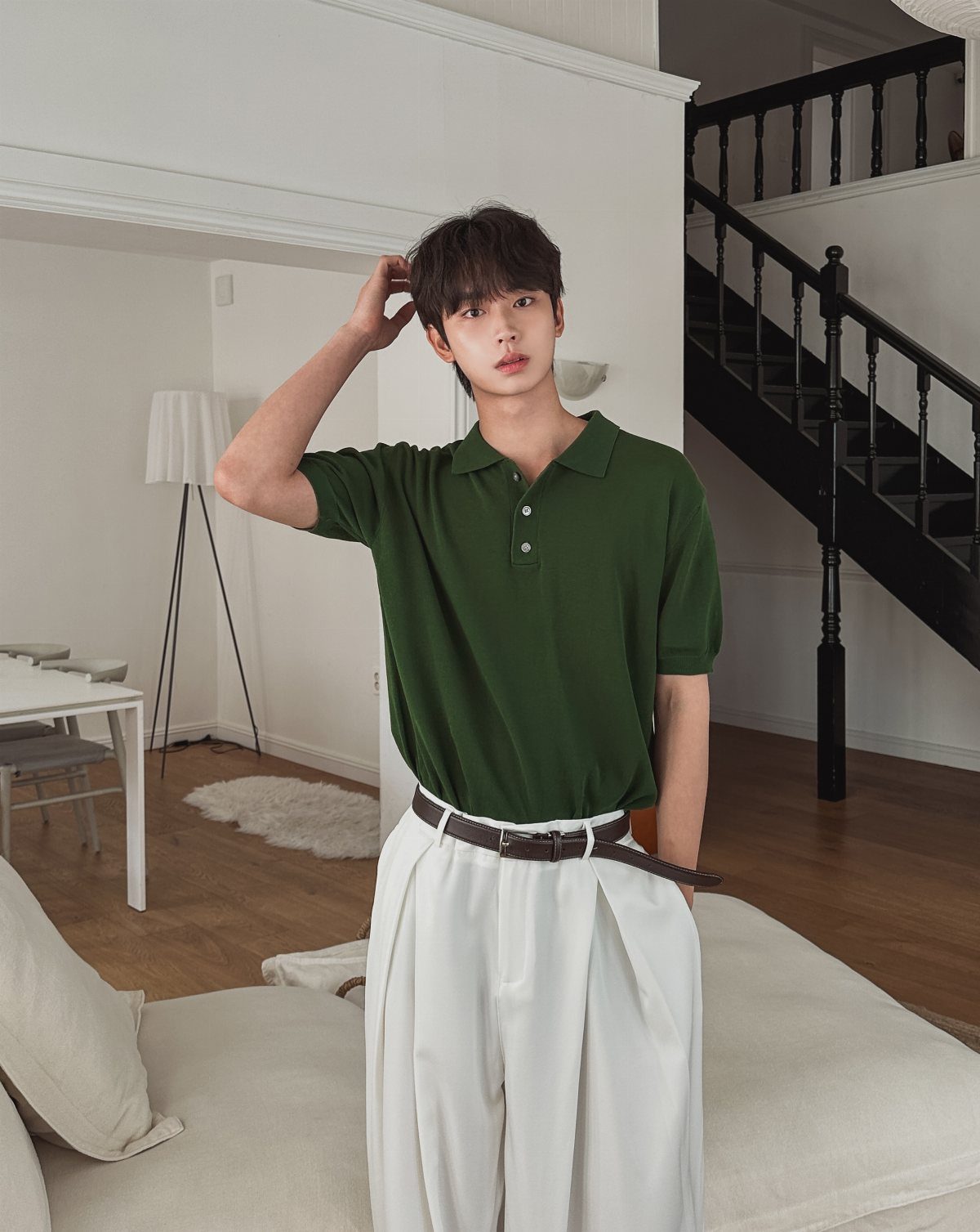 Young man posing in a green polo shirt and white high-waisted trousers indoors.