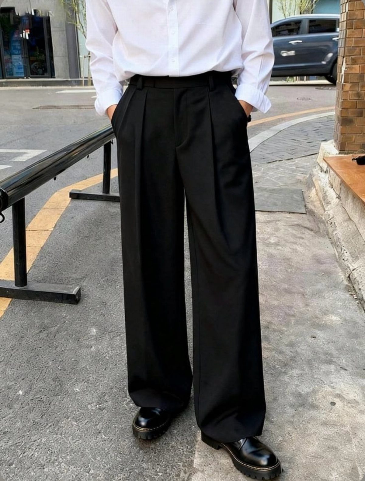 A person wearing white shirt, black wide-leg pleated trousers, and black leather shoes on a sidewalk.