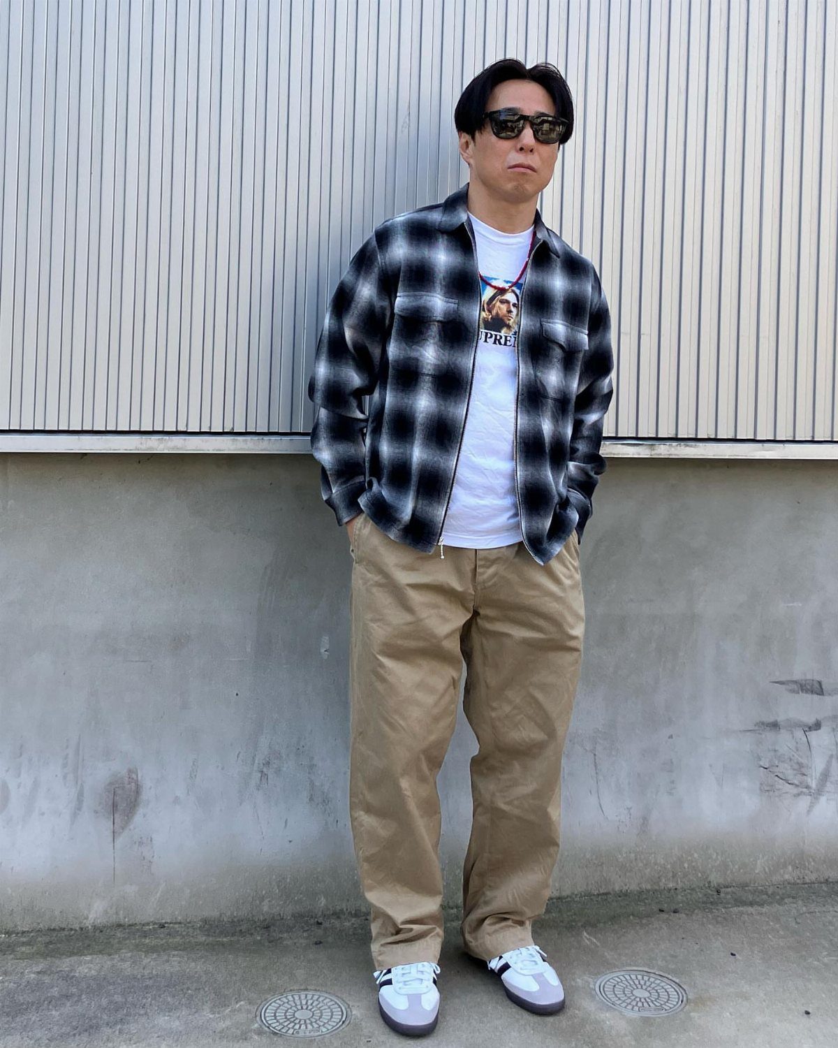 Man wearing a black and white checkered flannel shirt, white t-shirt, and tan trousers.
