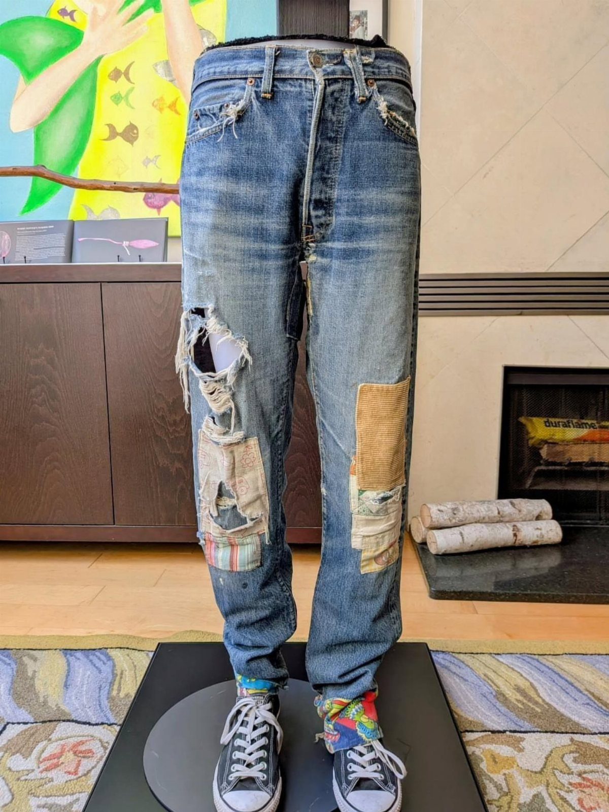 Blue denim jeans with large rips and various fabric patches displayed on a mannequin.