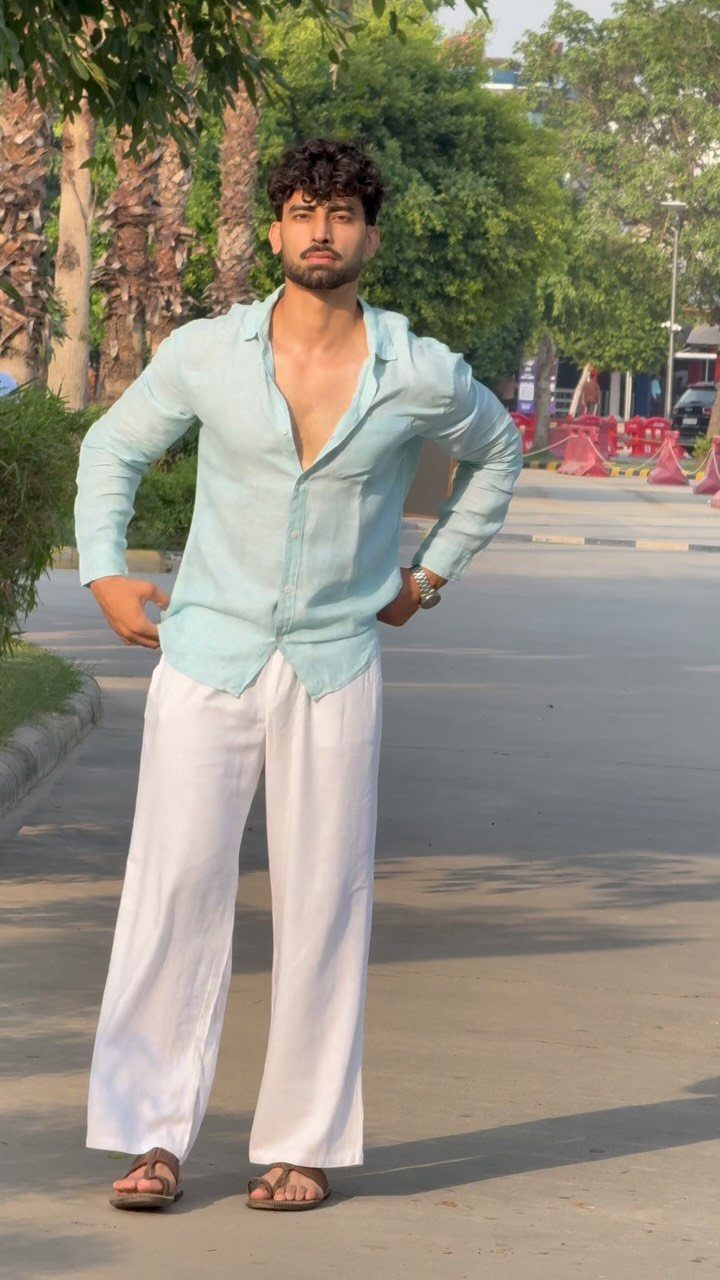 Man posing in a light blue linen shirt and wide-leg white linen pants outdoors.