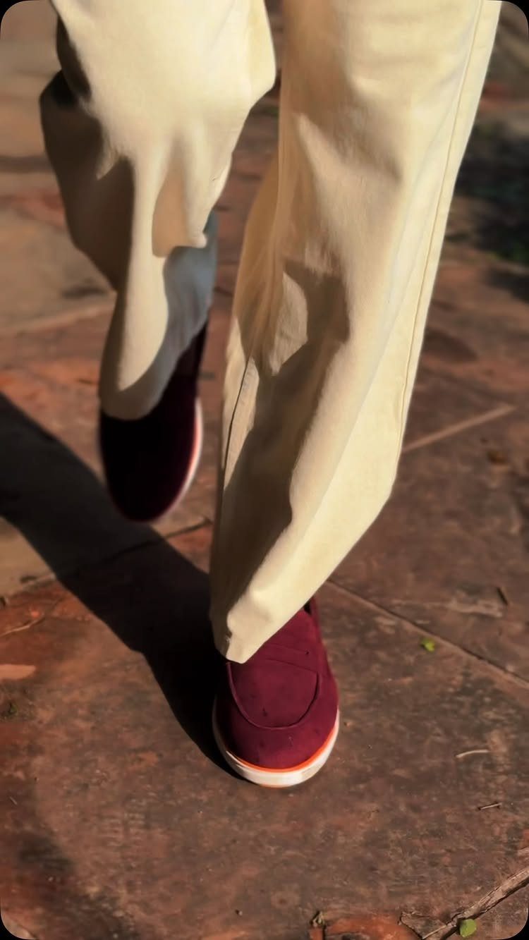 Person walking in cream trousers and burgundy slip-on loafers on a stone pavement.