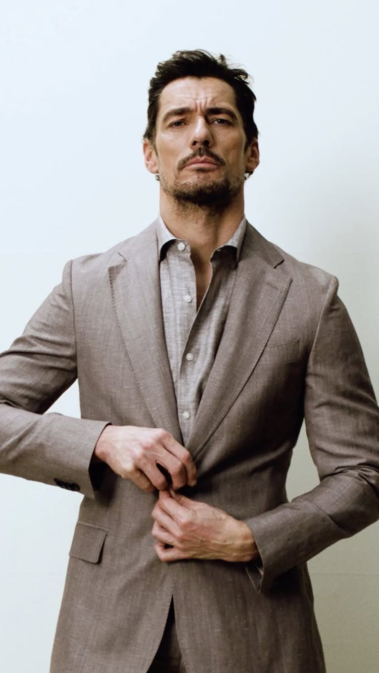 A man in a light brown linen suit jacket posing against a white background.