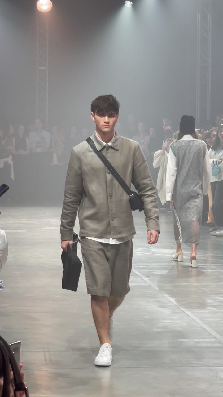 Male model walking a runway wearing a grey jacket and matching shorts.